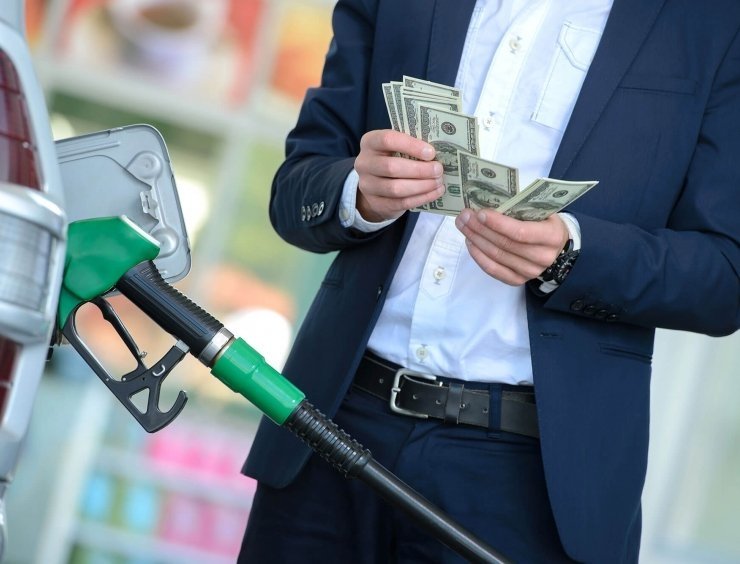  muž v obleku, který drží peníze a nalévá benzín.